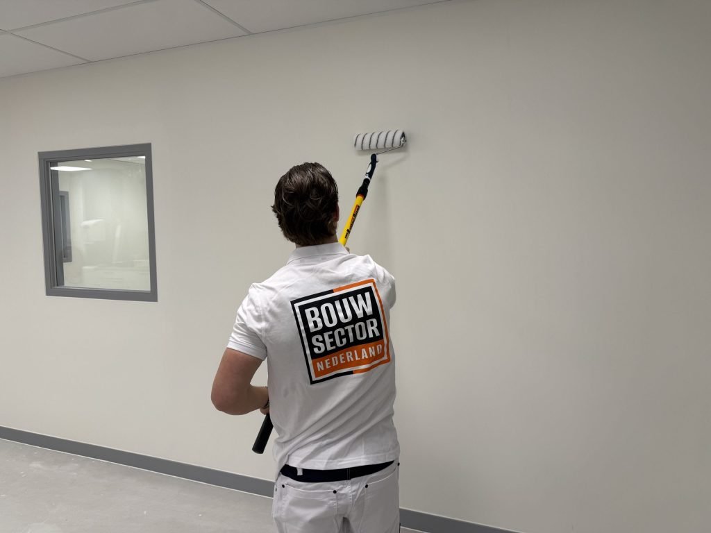 Schilder van Bouwsector Nederland rolt een lichte wand in een ruimte met een binnenraam en een systeemplafond