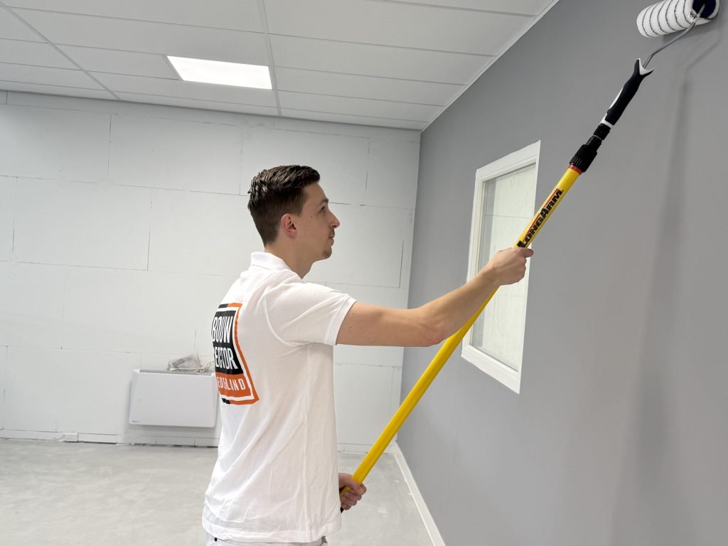 Schilder van Bouwsector Nederland rolt een grijze wand bij een raam in een kamer met een radiator