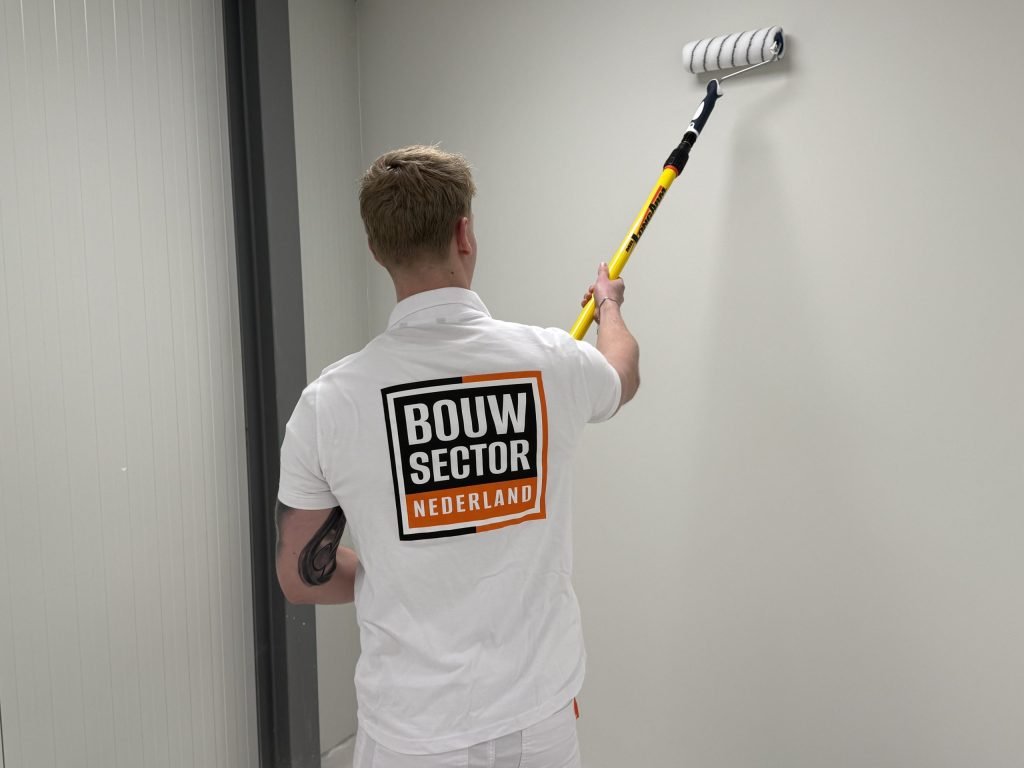 Schilder van Bouwsector Nederland rolt een lichte muur tot vlak onder het plafond in een smalle ruimte