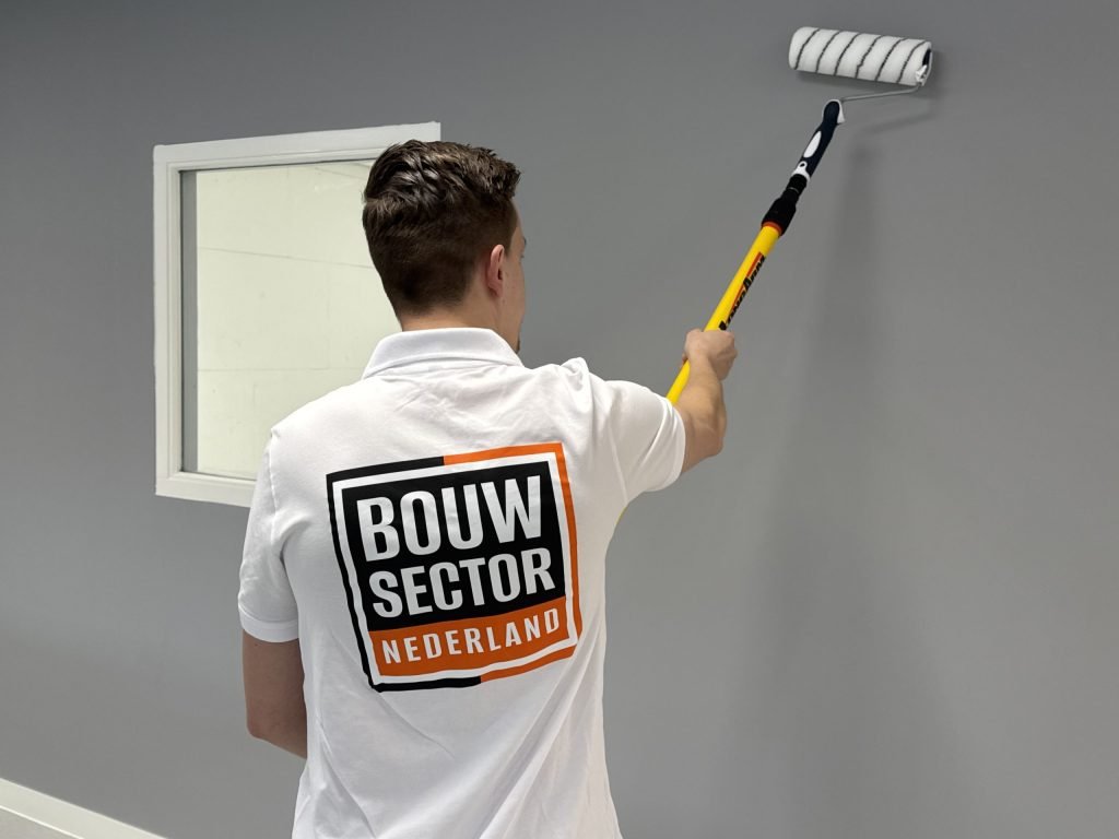 Schilder van Bouwsector Nederland rolt een grijze wand naast een raam met witte omlijsting